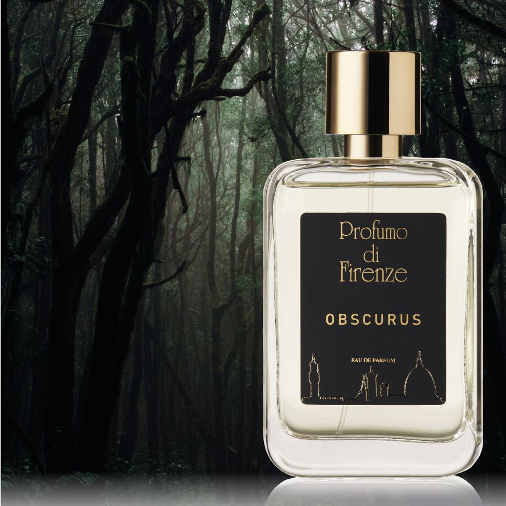 A bottle of Profumo Di Firenze OBSCURUS Eau de Parfum with a gold cap stands before a misty, dark forest. The black label with gold lettering and Florence landmarks hints at the perfume’s notes of sandalwood and incense.
