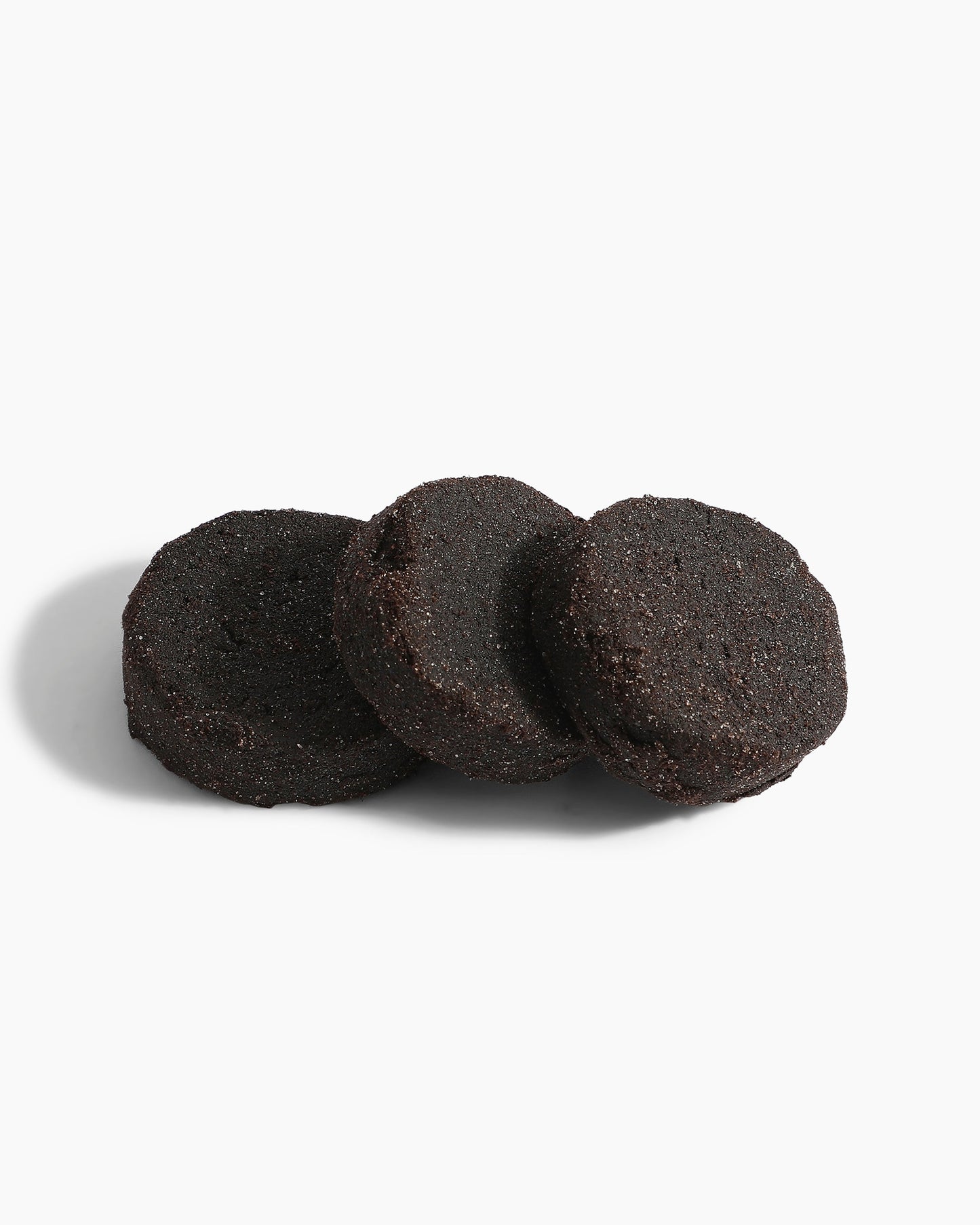 Three round, dark chocolate cookies are stacked on a plain white background with a soft shadow—an inviting scene reminiscent of the rich, alluring notes found in Hind Al Oud's Pink Smoke Dokhoon fragrance.