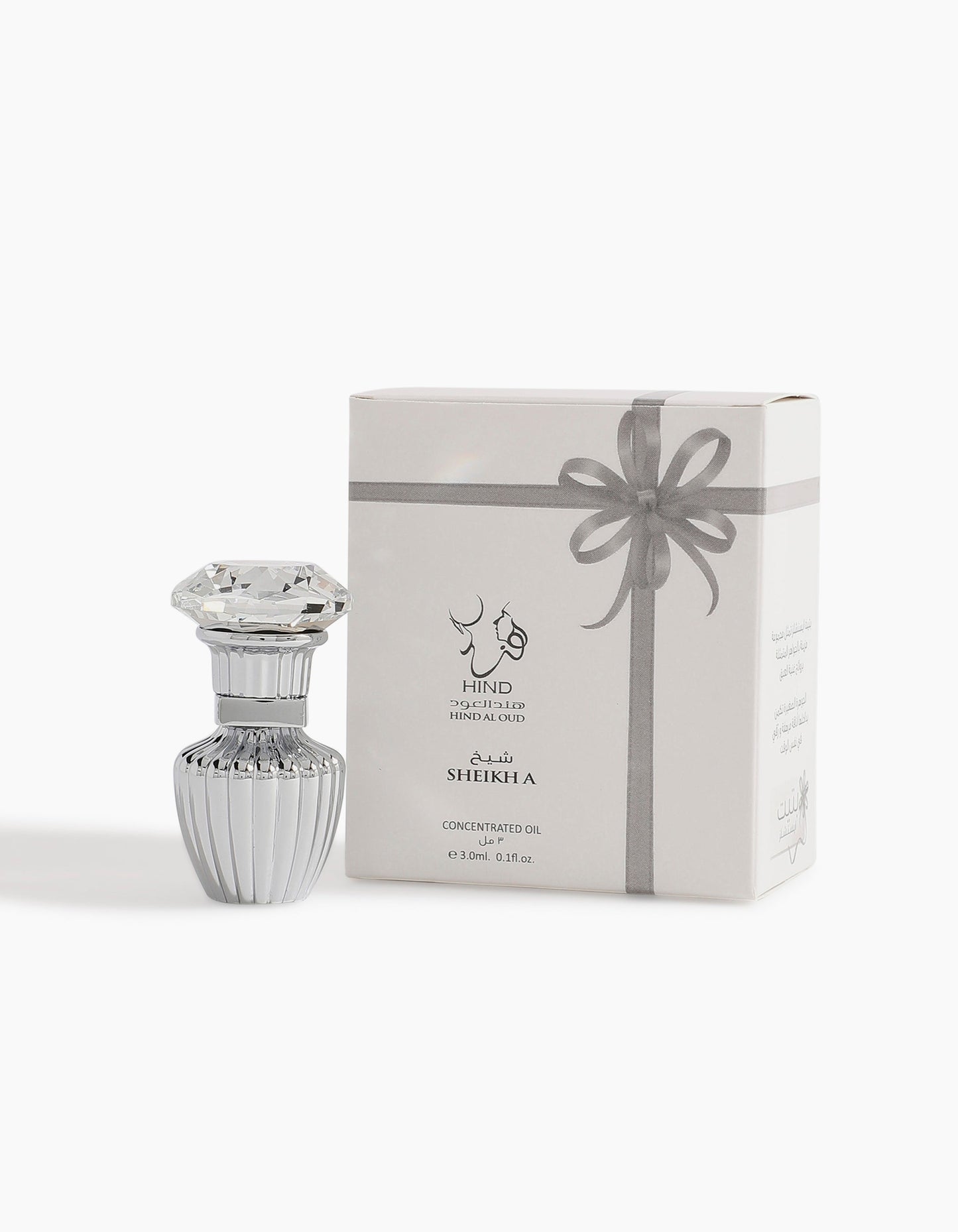 A decorative glass bottle with a gem-like lid stands next to a white box featuring silver Arabic and English text and a gray ribbon. Sheikh A Petite Concentrated Oil 3ml by Hind Al Oud exudes luxury with rare ambergris notes.