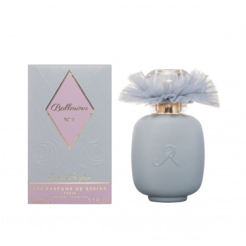 A pale blue perfume bottle with a sheer blue bow stands beside its matching box, labeled BALLERINA N°2 Eau de Parfum by LES PARFUMS DE ROSINE—a woody floral scent with magnolia. The box is pale blue with a pink diamond-shaped label.