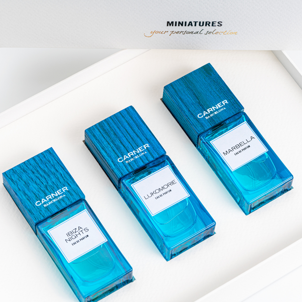 Three blue rectangular miniature perfumes from the MINIATURE SET DREAM COLLECTION by Carner Barcelona sit in a white tray. Above them, gold text reads "MINIATURES your personal selection," capturing Mediterranean inspiration. Brand: GIFTS.