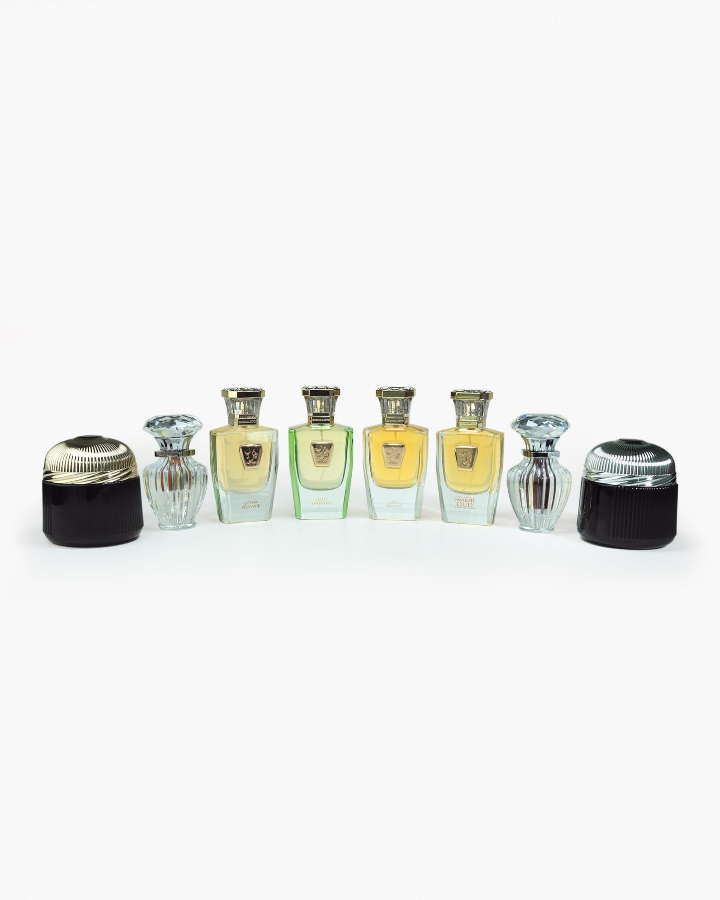 Seven elegant bottles from the Hind Al Oud Immortal Allure Collection Gift Set stand in a row against a white background, containing gold and green perfumes. Two bottles have ribbed designs, each topped with a decorative cap.