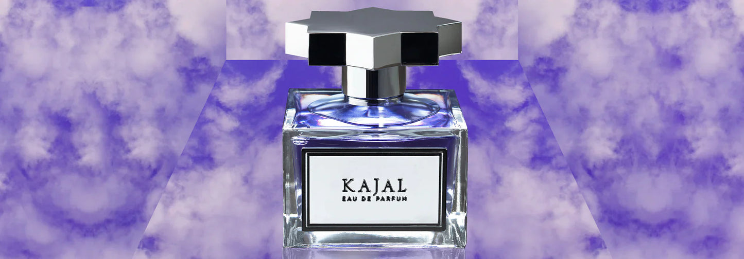 A bottle of Kajal - Eau de Parfum by Kajal Perfumes Paris, inspired by Arabic traditions and featuring Turkish Rose notes, sits against a dreamy purple cloudy background. Its elegant clear bottle has a geometric silver and black cap.