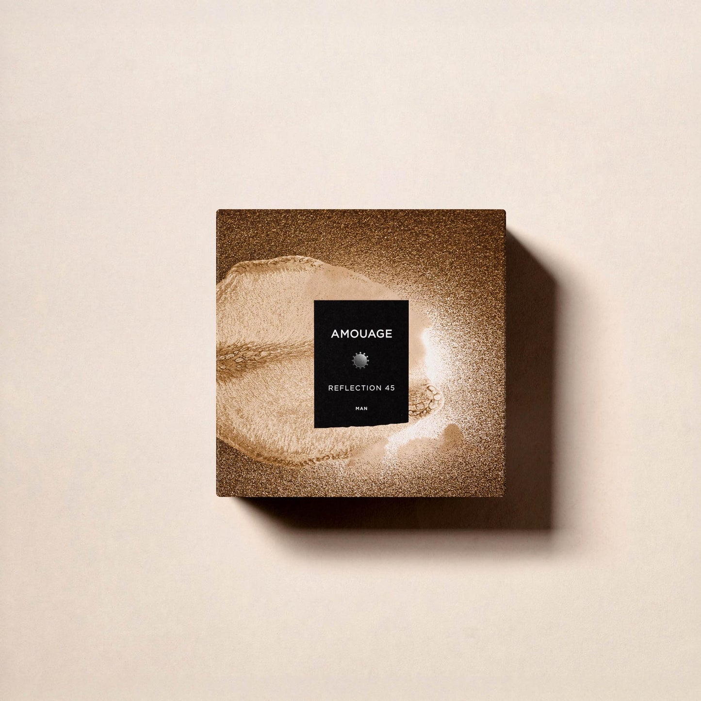A square, brown, textured box of Reflection 45 Man Extrait de Parfum by Fragrapedia Haus sits on a light beige surface, shadow to the right. Its black label with white text hints at the woody floral musk fragrance inside.