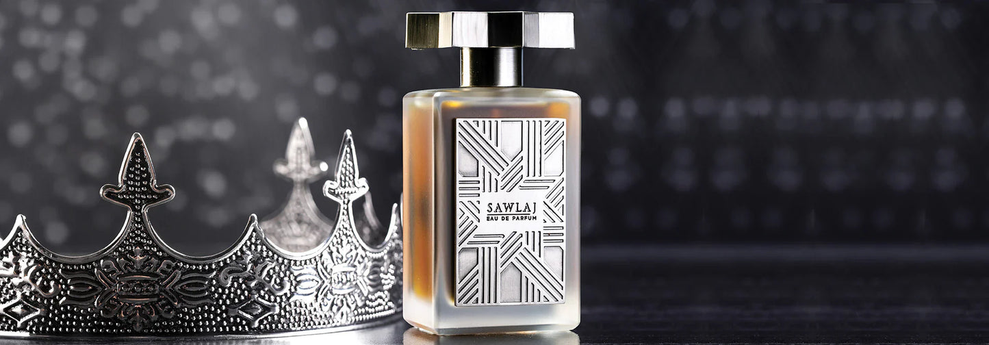 A silver crown rests beside a rectangular bottle of Sawlaj Eau de Parfum by Kajal Perfumes Paris, featuring a geometric label, set on a dark reflective surface with a blurred, mysterious backdrop that evokes enlightenment.