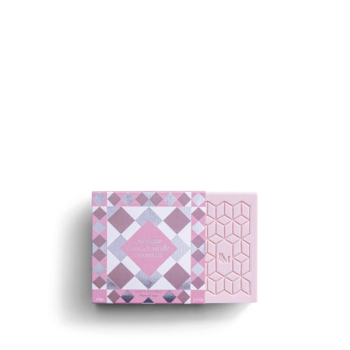 A pink and purple patterned ROSE ET MARIUS SCENTED SOAP box by Rose Et Marius, partially open to show a geometric pink soap bar embossed with “M,” sits against a white background.