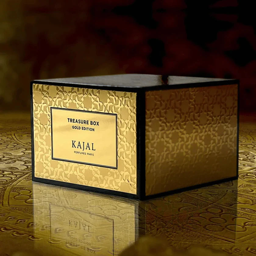 A gold Kajal Gold Treasure Box Discovery Kit by Kajal Perfumes Paris rests on a gold-engraved surface, presenting a travel-size set of luxury fragrances in an opulent setting.