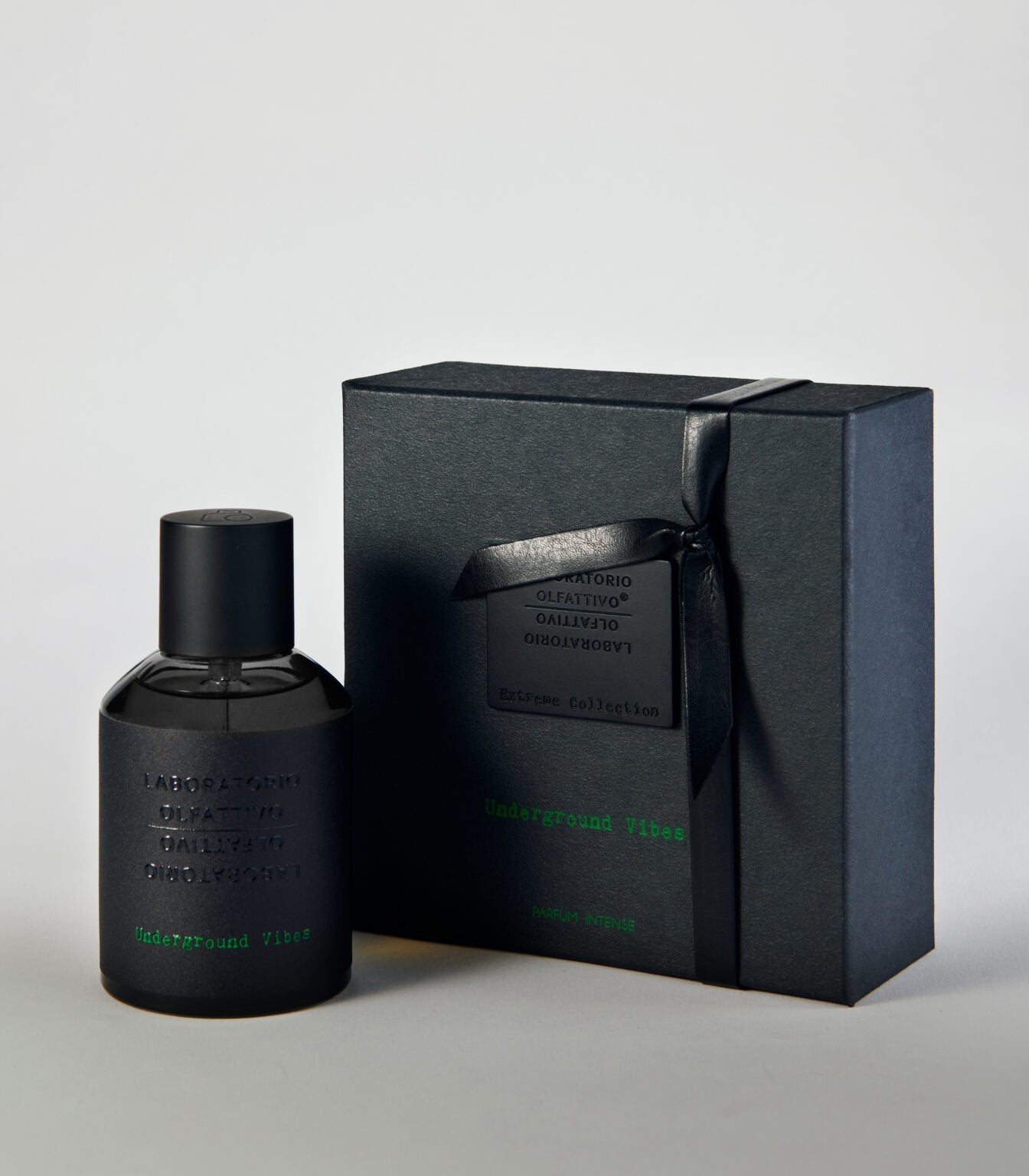 A black bottle of Underground Vibes - Laboratorio Olfattivo perfume stands by its matching ribbon-tied black box. The embossed packaging with green accents hints at the unique scent crafted by Laboratorio Olfattivo.