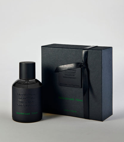 A black bottle of Underground Vibes - Laboratorio Olfattivo perfume stands by its matching ribbon-tied black box. The embossed packaging with green accents hints at the unique scent crafted by Laboratorio Olfattivo.