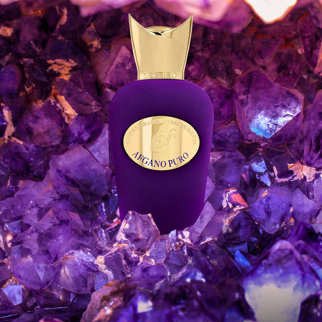 A purple SOSPIRO Afgano Puro Eau de Parfum bottle with a gold cap is displayed among vibrant purple crystals, suggesting a luxurious tobacco vanilla fragrance.