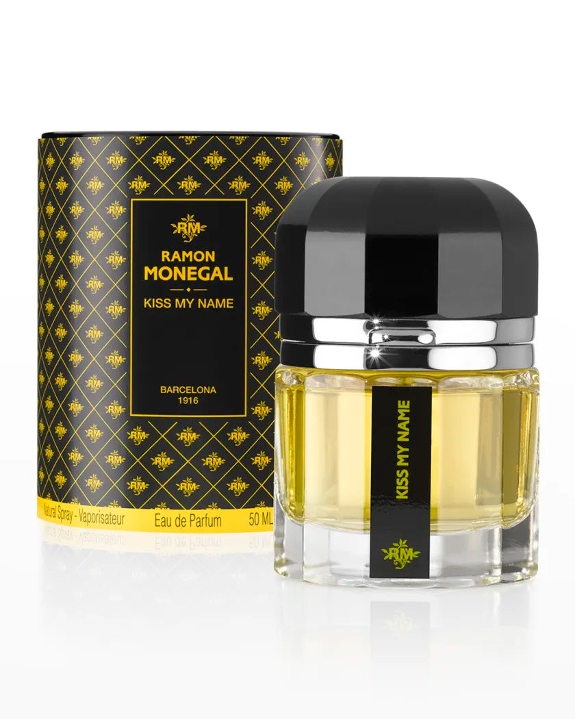 A bottle of Kiss My Name Eau de Parfum by Ramon Monegal is displayed before its yellow and black patterned box, both featuring labels with the fragrance name and brand, showcasing the elegance of Ramon Monegal.