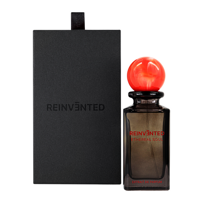 A black perfume box labeled REINVĒNTED stands beside a dark glass bottle with a red marbled cap and red text reading "ETHEREAL SOUL Extrait de Parfum - REINVENTED," a celestial scent by REINVĒNTED with fruity oriental allure.