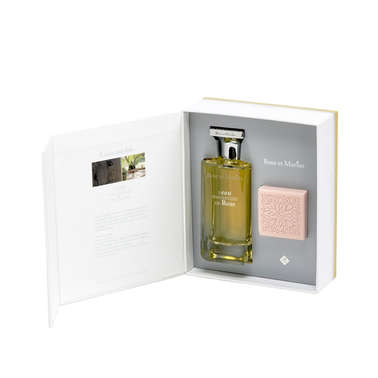 The Rose Et Marius GIFT SET BASKING IN THE SUN WITH MARIUS features a glass Eau Centifolia Rose perfume bottle and a pink, patterned soap, beautifully presented in an open box with printed text inside the lid.