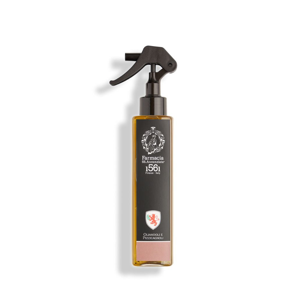 A rectangular spray bottle with a black trigger nozzle and dark label displays "Farmacia SS. Annunziata 1561" and "Oliandoli e Pizzicagnoli Room Spray – Farmacia." Inside is an invigorating, light amber olive room spray.