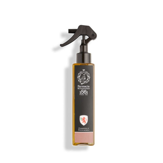 A rectangular spray bottle with a black trigger nozzle and dark label displays "Farmacia SS. Annunziata 1561" and "Oliandoli e Pizzicagnoli Room Spray – Farmacia." Inside is an invigorating, light amber olive room spray.