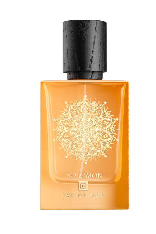 A rectangular amber bottle with a black wooden cap, detailed gold mandala, and SOLOMON plus Eau De Moe on the front. This 80ML men's fragrance, SOLOMON Eau de Parfum by Eau De Moe, exudes refined elegance.