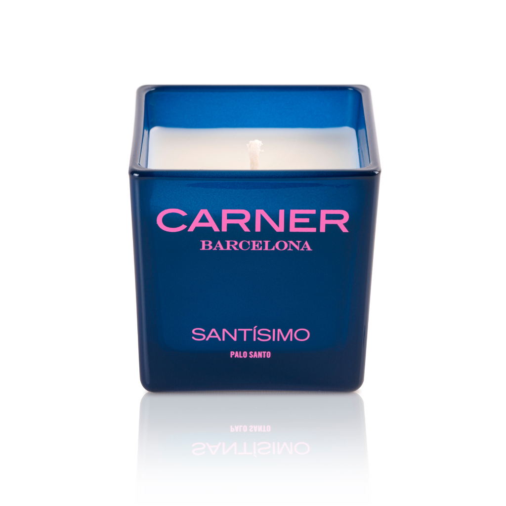 A blue square SANTÍSIMO CANDLE by Carner, featuring a white candle inside, evokes the soothing aroma of guaiac wood and musk—ideal for an incense-inspired experience.