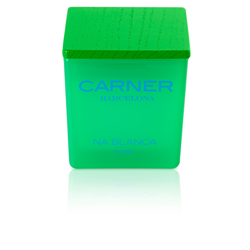 A green square candle with a matching textured cap captures the Formentera vibe. The label says NA BLANCA CANDLE - Carner Barcelona by GIFTS in blue, with the candle reflected on a white surface.