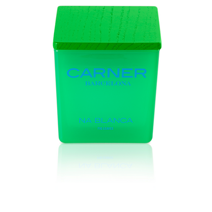 A green square candle with a matching textured cap captures the Formentera vibe. The label says NA BLANCA CANDLE - Carner Barcelona by GIFTS in blue, with the candle reflected on a white surface.