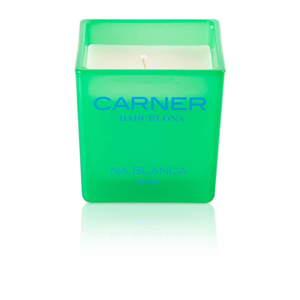 A green square candle holder with a white candle inside, labeled NA BLANCA CANDLE - Carner Barcelona by GIFTS, recalls the fresh scent of fig trees and memories of Formentera.