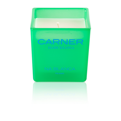 A green square candle holder with a white candle inside, labeled NA BLANCA CANDLE - Carner Barcelona by GIFTS, recalls the fresh scent of fig trees and memories of Formentera.