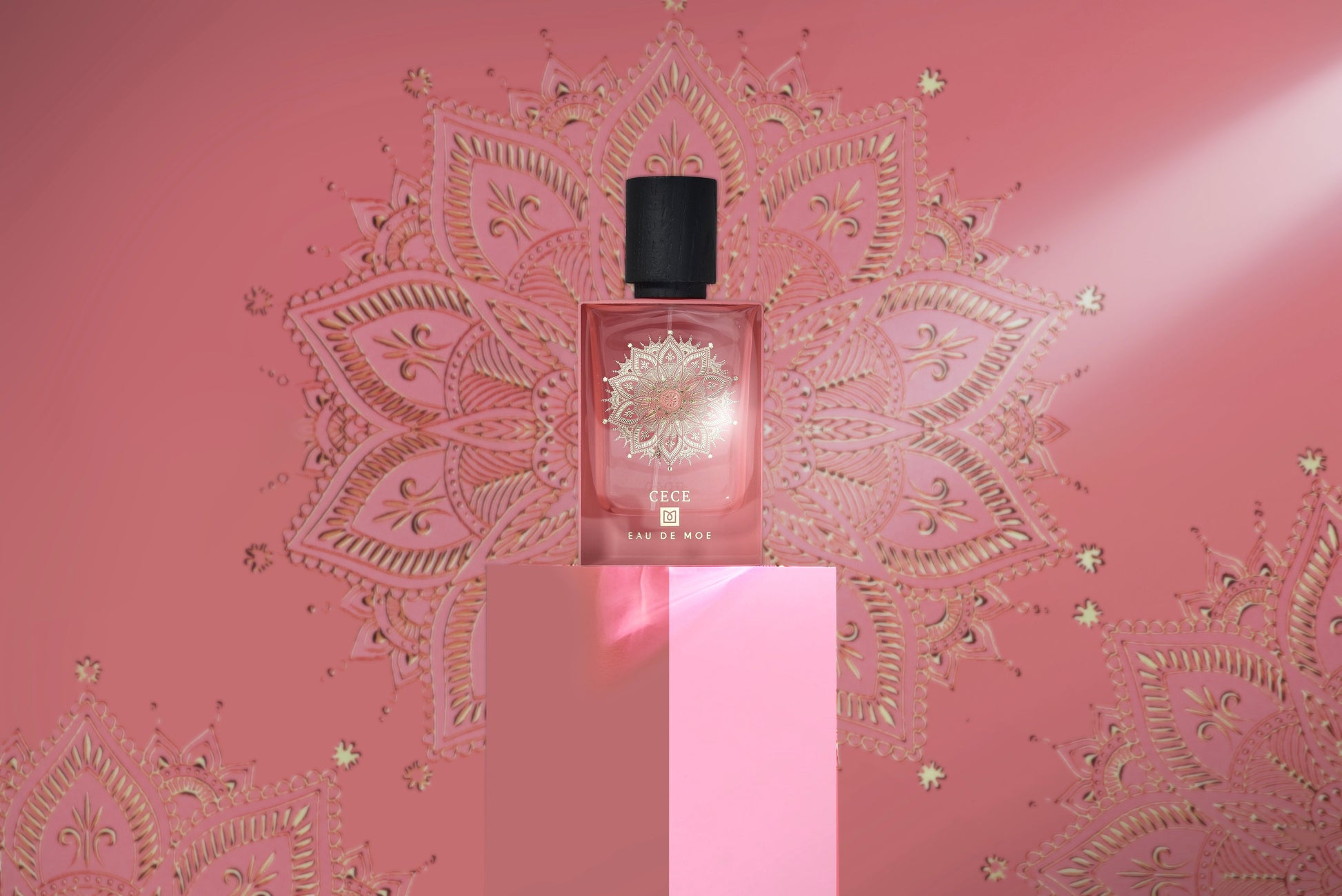A bottle of Eau De Moe’s CECE Eau de Parfum with a black cap stands on a pink pedestal against a pink backdrop decorated with gold mandala designs, highlighted to showcase the fragrance's elegance and luxury.