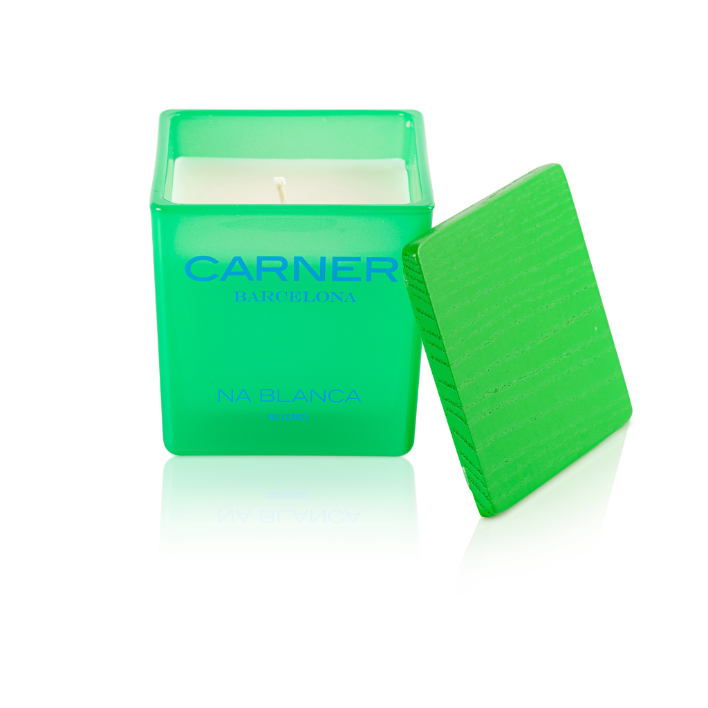 A green square NA BLANCA CANDLE by GIFTS, inspired by Formentera fig trees, comes with a wood-textured lid labeled Carner Barcelona, shown resting beside the candle.