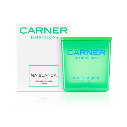 A green glass NA BLANCA CANDLE by GIFTS rests beside its white box, adorned with blue and green text. Inspired by Formentera, this fig tree-scented candle captures the island’s fresh, leafy aroma.