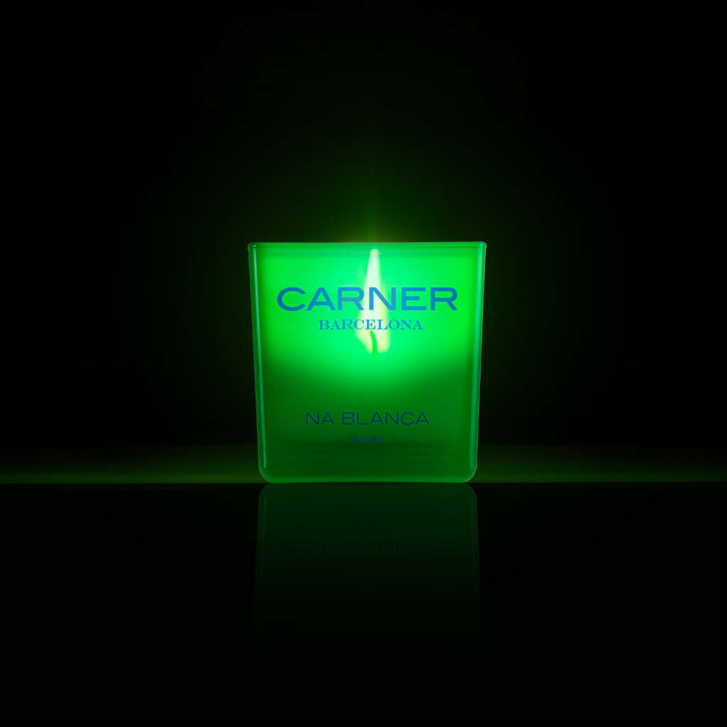 A green NA BLANCA CANDLE by GIFTS glows brightly, casting fig tree-inspired reflections on a shiny surface and evoking memories of tranquil Formentera nights.
