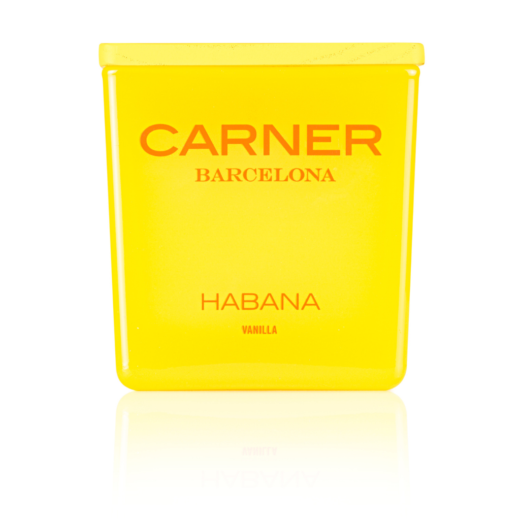 A vibrant yellow GIFTS HABANA CANDLE by Carner Barcelona stands upright, labeled with bold orange "HABANA VANILLA," its reflection shimmering on the surface below.