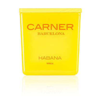 A vibrant yellow GIFTS HABANA CANDLE by Carner Barcelona stands upright, labeled with bold orange "HABANA VANILLA," its reflection shimmering on the surface below.