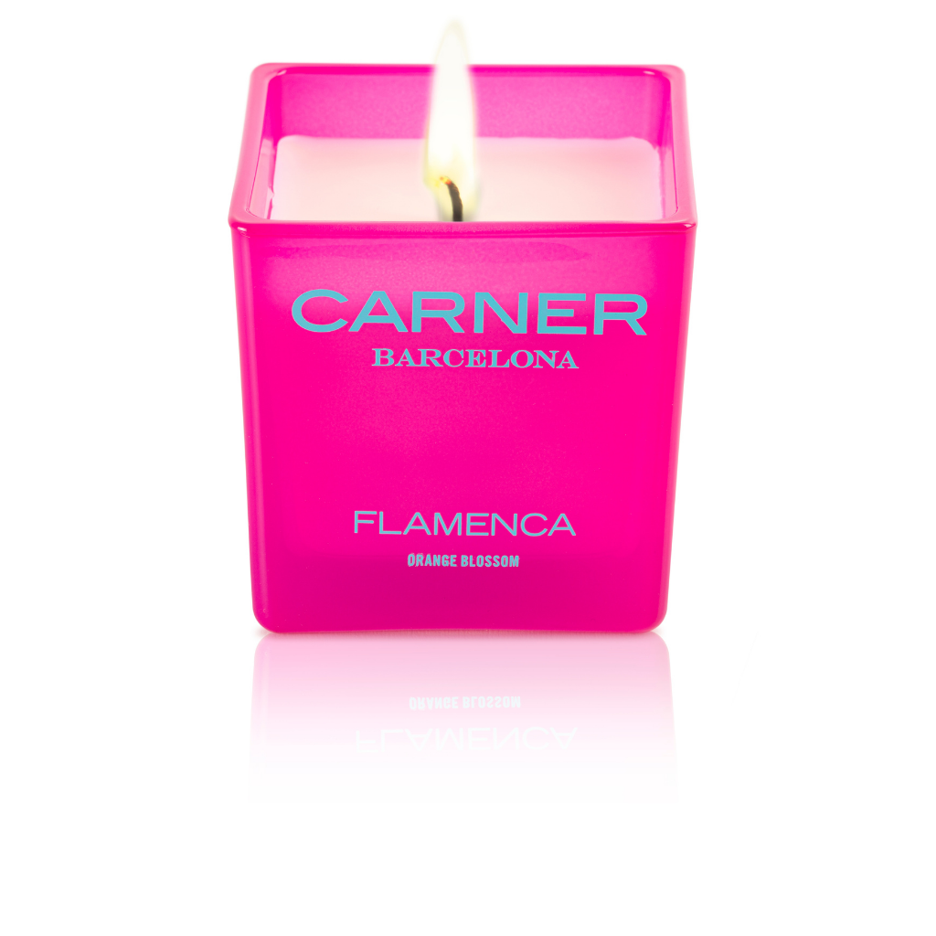 A lit pink square FLAMENCA CANDLE by GIFTS (Carner Barcelona) in a glass holder sits against a white background; the label reads Flamenca Orange Blossom.