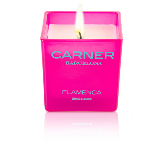A lit pink square FLAMENCA CANDLE by GIFTS (Carner Barcelona) in a glass holder sits against a white background; the label reads Flamenca Orange Blossom.