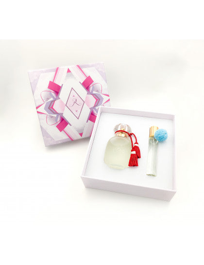 The COFFRET "SWIZ" by LES PARFUMS DE ROSINE is a gift box with a pink and white ribbon lid, holding Rose Griotte limited edition perfume in a round bottle with red tassel and a small spray vial with blue pom-pom, nestled in white foam.