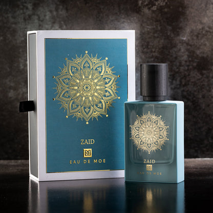 A blue ZAID Eau de Parfum 80ML bottle by Eau De Moe stands before its matching box, both featuring a gold mandala on teal, set against a dark backdrop. Experience the allure of ZAID Eau de Parfum.