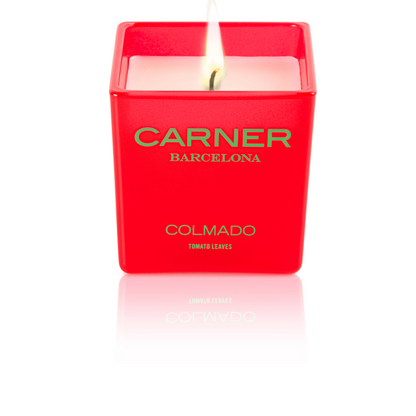 A lit COLMADO CANDLE by GIFTS (Carner Barcelona) glows above white wax in a square container labeled TOMATO LEAVES.