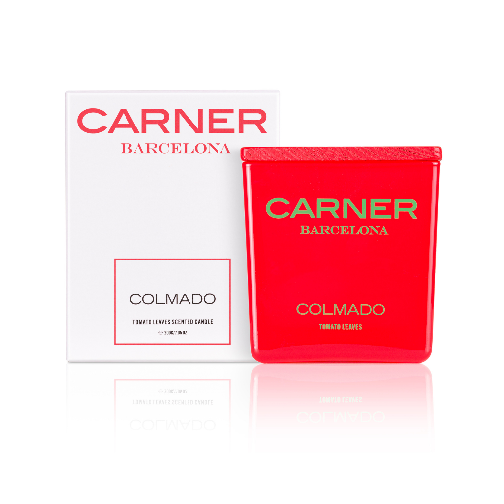 A GIFTS COLMADO CANDLE by Carner Barcelona labeled Tomato Leaves sits beside its matching red and white box, both featuring the brand and scent name, elegantly reflected on a white surface.