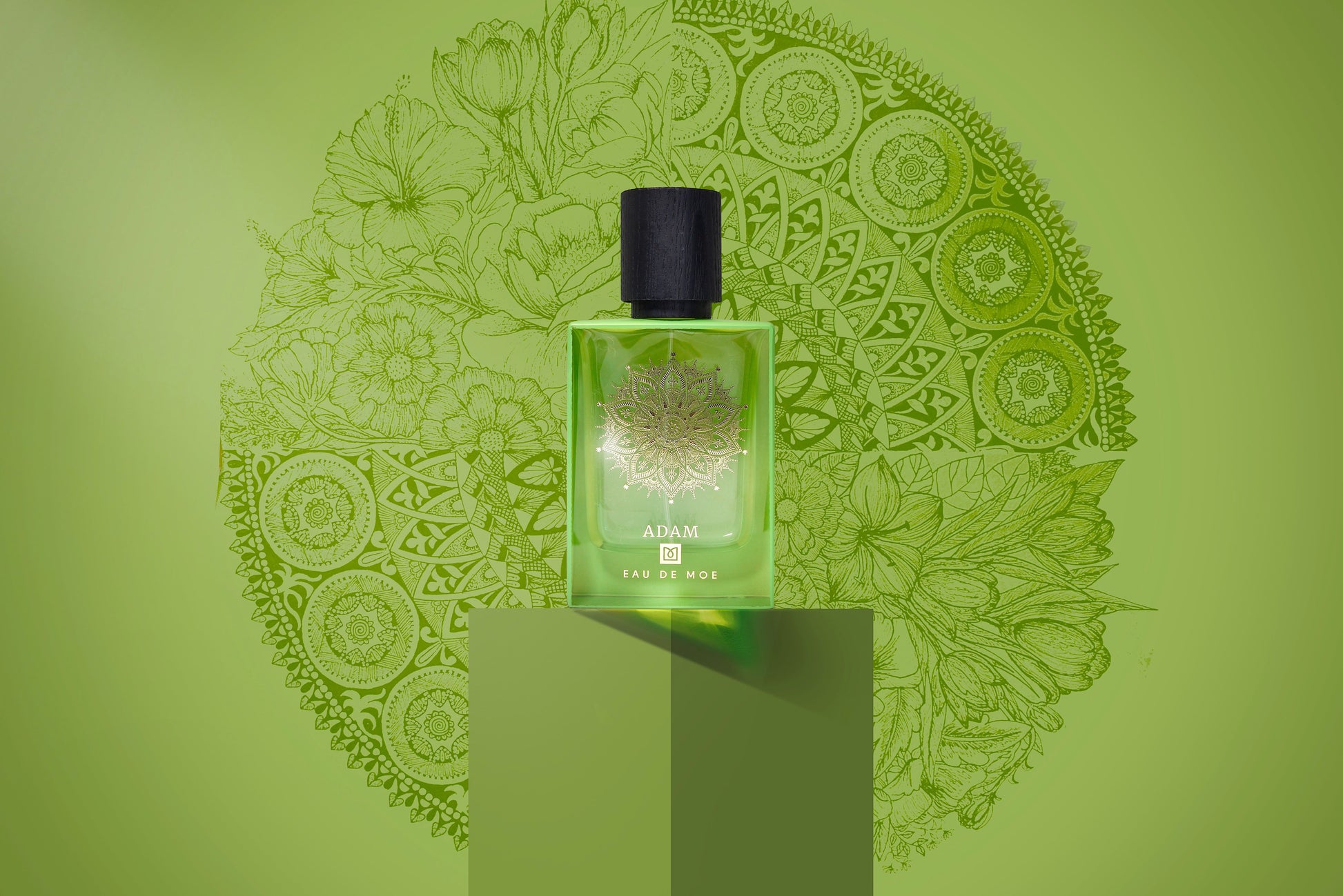 A green perfume bottle labeled ADAM Eau de Parfum by Eau De Moe rests on a matching pedestal, set against intricate floral and geometric patterns—an elegant men's fragrance with notes of Italian bergamot.