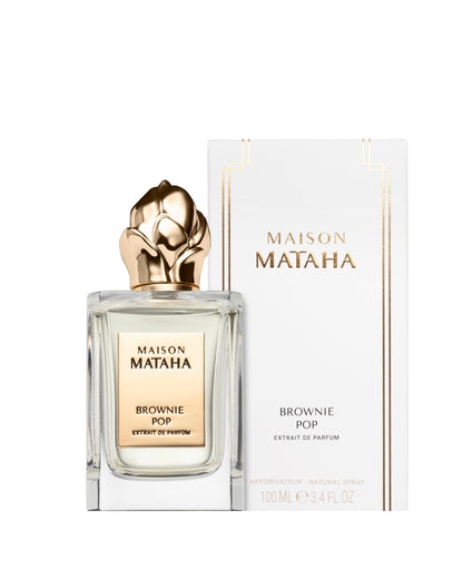 A Fragrapedia Haus Brownie Pop Extrait de Parfum bottle with a gold floral cap is placed before its white and gold box, both featuring the brand name and product details, evoking the gourmet brownie scent.