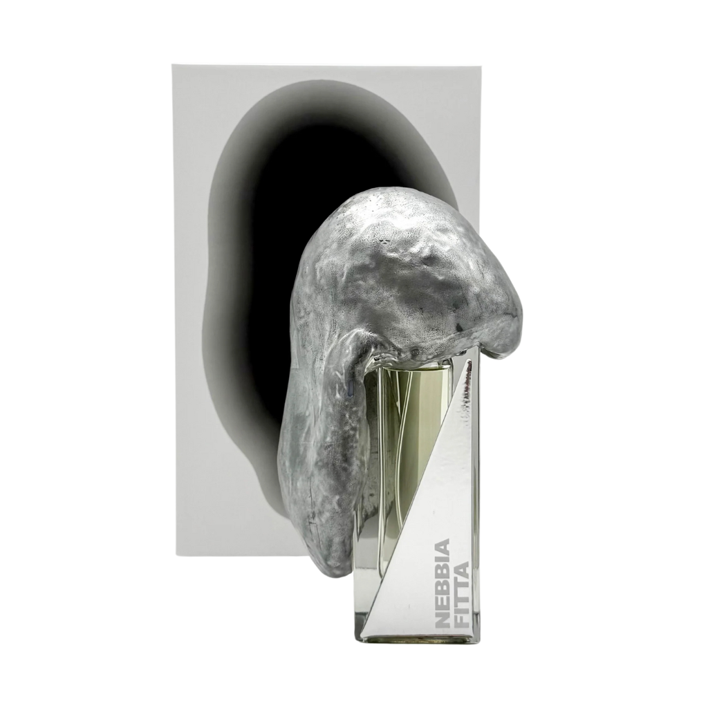 The NEBBIA FITTA "thick fog" Eau de Parfum by Filippo Sorcinelli is a clear glass bottle, partially veiled by a metallic silver sculpture. Oakmoss notes are suggested, while a white background and gray shadow lend modern elegance.