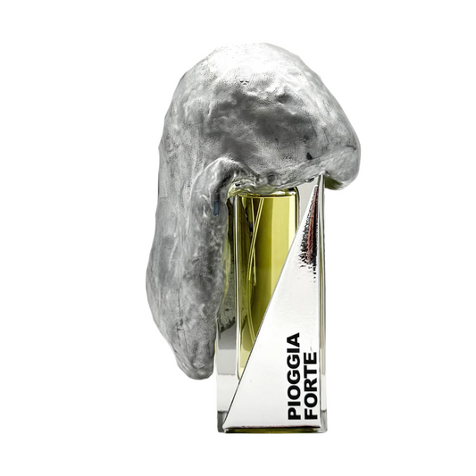 The PIOGGIA FORTE "heavy rain" Eau de Parfum by Filippo Sorcinelli features a silver metallic abstract sculpture draped across the bottle, with glimpses of glass and mirrored surfaces reflecting the fragrance’s artistry.