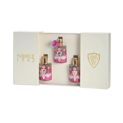 A cream-colored BON BON - Nobile 1942 gift box by Nobile 1942 with gold logos and sliding panels holds three fairy tale fragrances in pink-labeled bottles, beautifully arranged in a row.