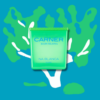 A green NA BLANCA CANDLE by Carner Barcelona from GIFTS is centered against a blue background with abstract white and green shapes resembling fig tree leaves.