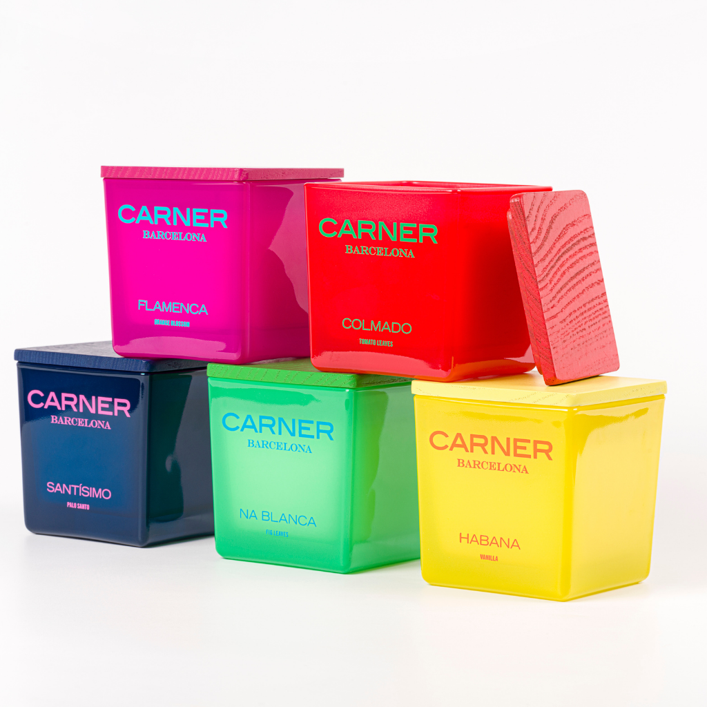 Five vibrant GIFTS FLAMENCA CANDLEs by Carner Barcelona are pyramid-stacked: dark blue (Santísimo), pink (Flamenca), green (Na Blanca), yellow (Habana), and red (Colmado)—each topped with a wooden lid.
