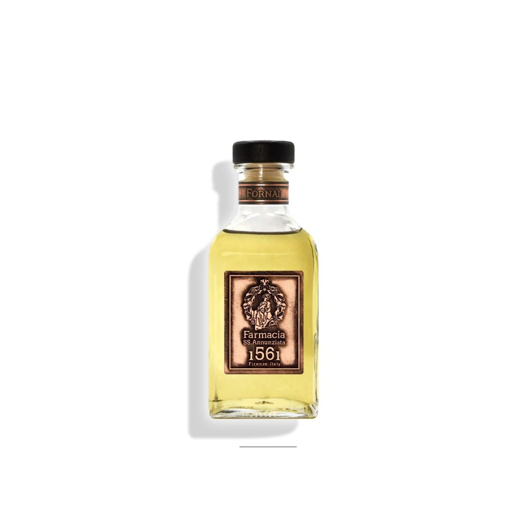 The Fornai DIFFUSER - Farmacia by Farmacia SS. Annunziata 1561 features a clear glass bottle with light yellow cinnamon vanilla fragrance, black cap, and a vintage-style emblem label. It casts a shadow on a white background.