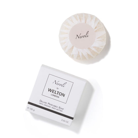 A round, wrapped bar of Welton London NEROLI DELUXE PERFUMED SOAP WITH ORGANIC SHEA BUTTER, 3.52 oz., made in France for sensitive skin, rests above its white box on a white background.