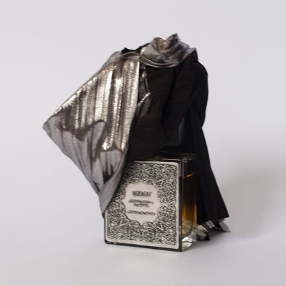 The UNUM _QUANDO_RAPITA_IN_ESTASI_ "when wrapped in ecstasy" EDP by Filippo Sorcinelli features a glass bottle with an ornate black and white label, draped in black and silver fabric, evoking operatic elegance and rich sandalwood notes.