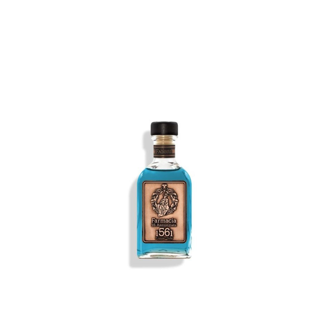 A small glass Fabbri DIFFUSER by Farmacia SS. Annunziata 1561, filled with blue liquid and black reeds, features a black cap and tan label with an ornate emblem, "Farmacia," and "1561," centered on a white background.