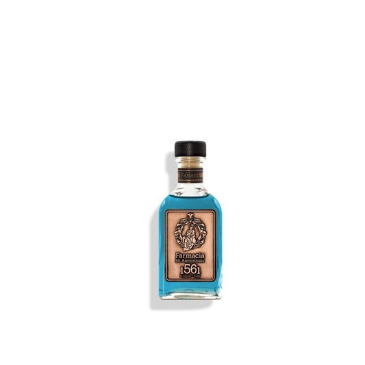 A small glass Fabbri DIFFUSER by Farmacia SS. Annunziata 1561, filled with blue liquid and black reeds, features a black cap and tan label with an ornate emblem, "Farmacia," and "1561," centered on a white background.
