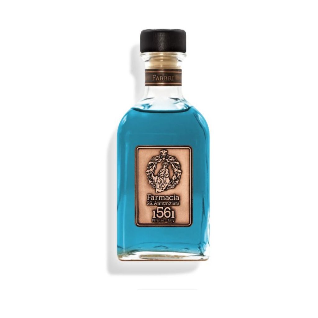 A clear glass bottle with blue liquid, a gold and brown Farmacia SS. Annunziata 1561 label, black cap with gold Fabbri band, and black reeds—Fabbri DIFFUSER - Farmacia: an elegant home fragrance diffuser.